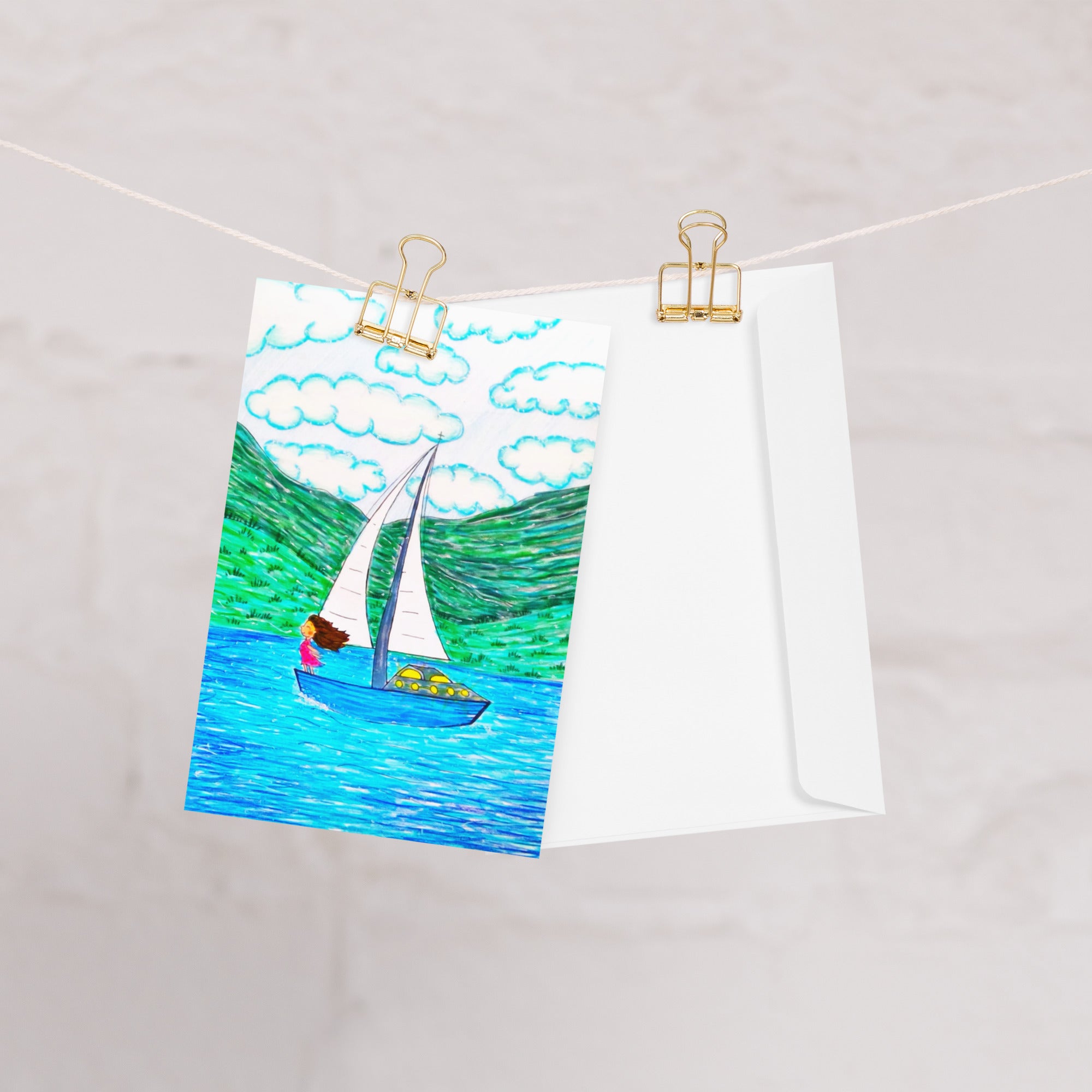 A rectangular greeting card, featuring a colourful illustration of a sailboat on blue water with green hills and white clouds. The left side of the card is plain white with the AllThingsGoode logo.
