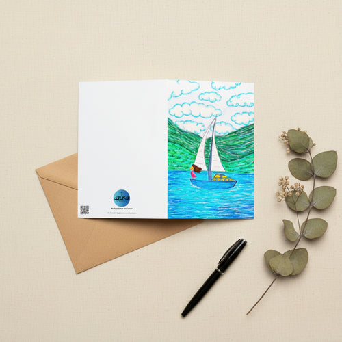 A rectangular greeting card, featuring a colourful illustration of a sailboat on blue water with green hills and white clouds. The left side of the card is plain white with the AllThingsGoode logo.