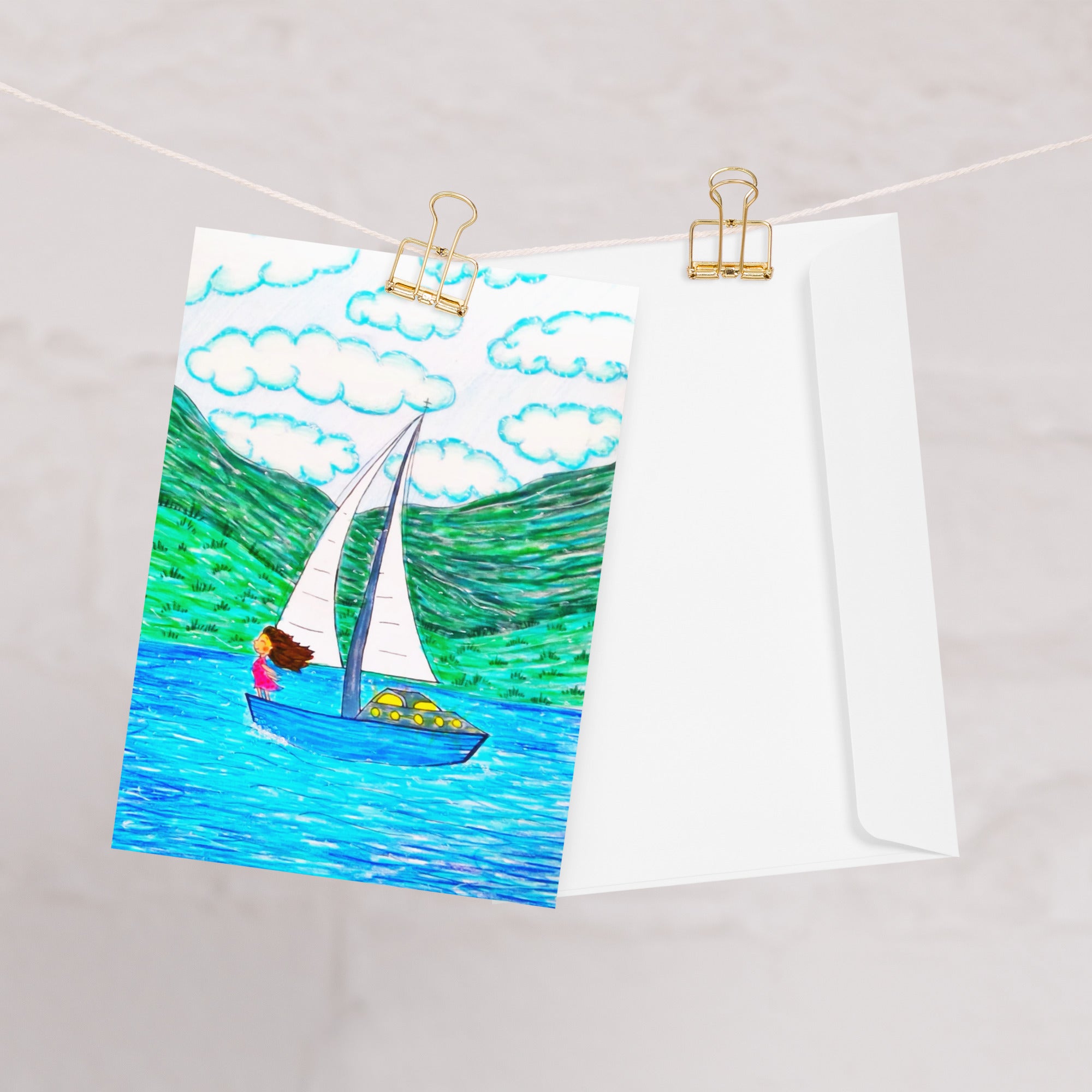 A rectangular greeting card, featuring a colourful illustration of a sailboat on blue water with green hills and white clouds. The left side of the card is plain white with the AllThingsGoode logo.